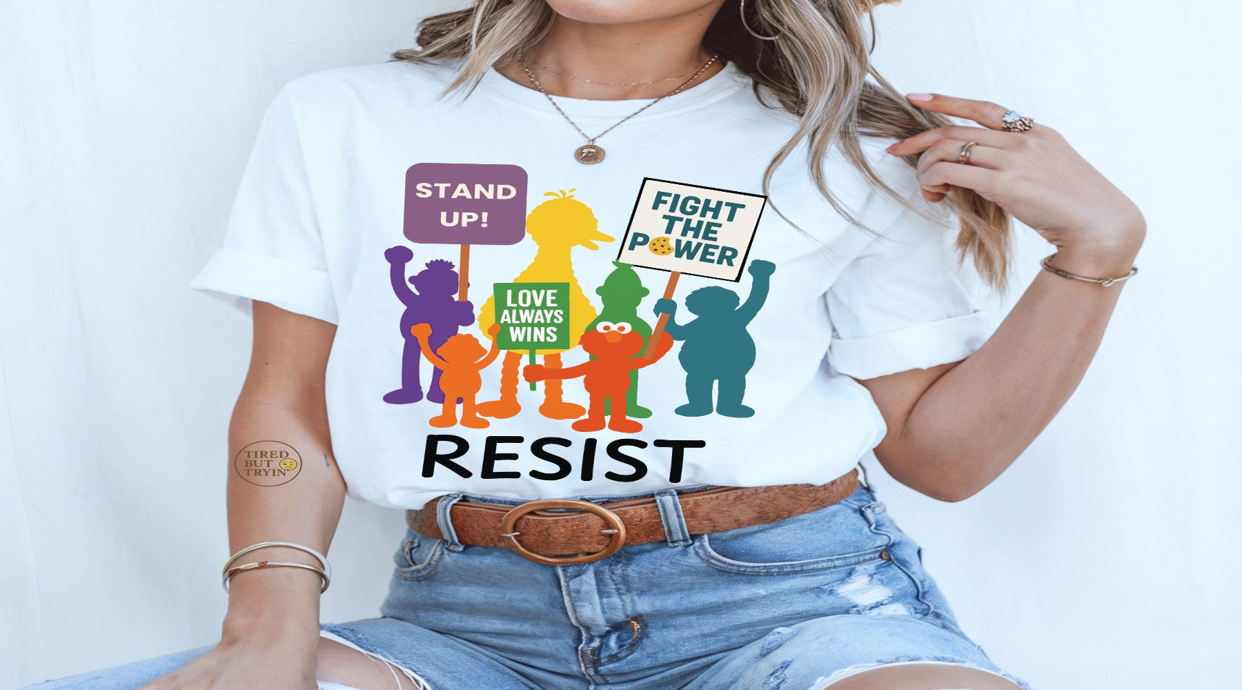 Person wearing a white t-shirt with colorful graphic and text 'STAND UP!', 'FIGHT THE POWER', 'LOVE ALWAYS WINS', and 'RESIST'.
